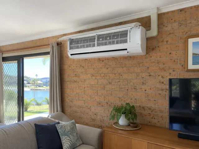 Clean split system indoor head on a brick living room wall with open front panel and visible filters in Runaway Bay