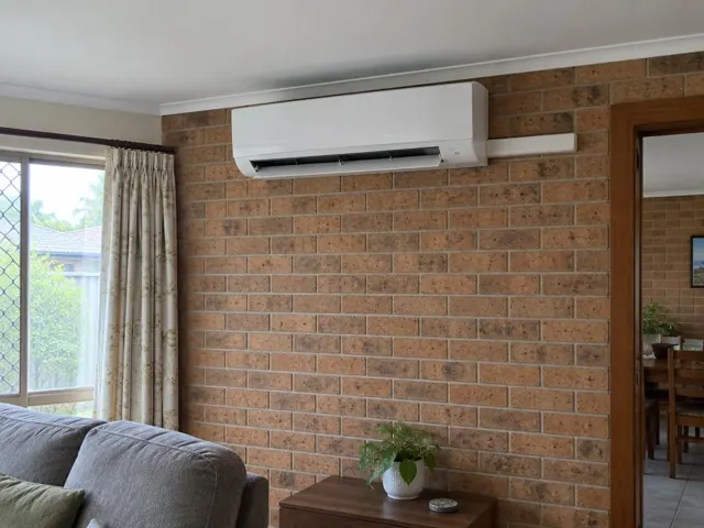 Wall-mounted split system on a brick feature wall in a living room with louvre open in Labrador