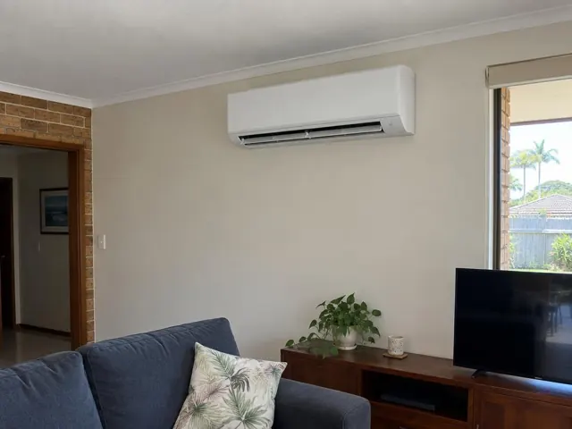 Wall-mounted split system high on a beige living room wall above a sideboard in Runaway Bay